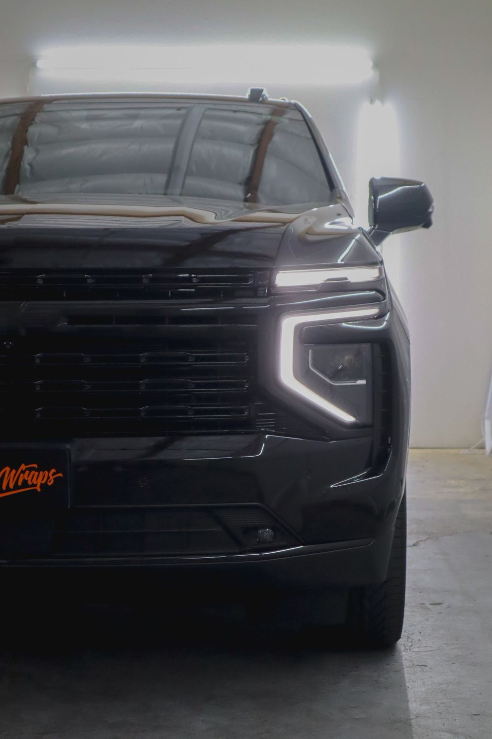 Headlight and grille close-up on a Chevrolet Tahoe High Country with gloss black chrome delete by Drift Wraps
