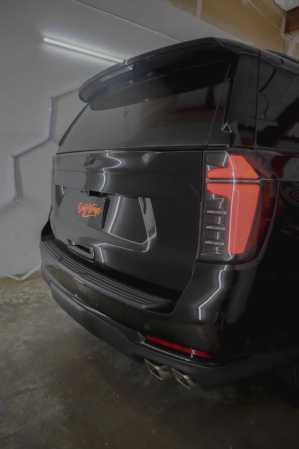 Blacked-out rear bowtie emblem and taillight on a Chevrolet Tahoe High Country with gloss black chrome delete by Drift Wraps