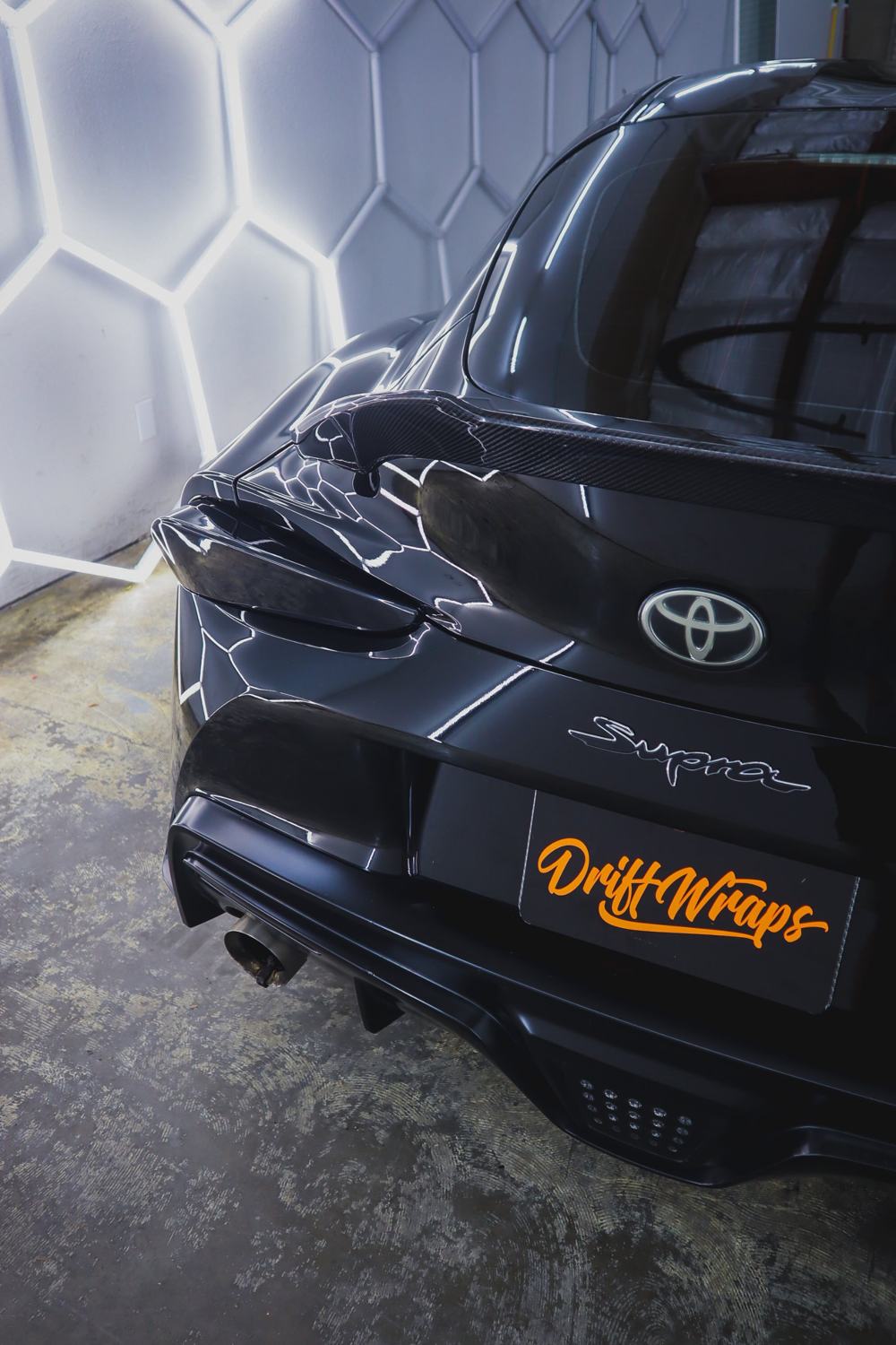 Rear of a black 2020 Toyota GR Supra wrapped in Gloss Black Obsidian color PPF by Drift Wraps in Rancho Cordova, shot under hexagon shop lights