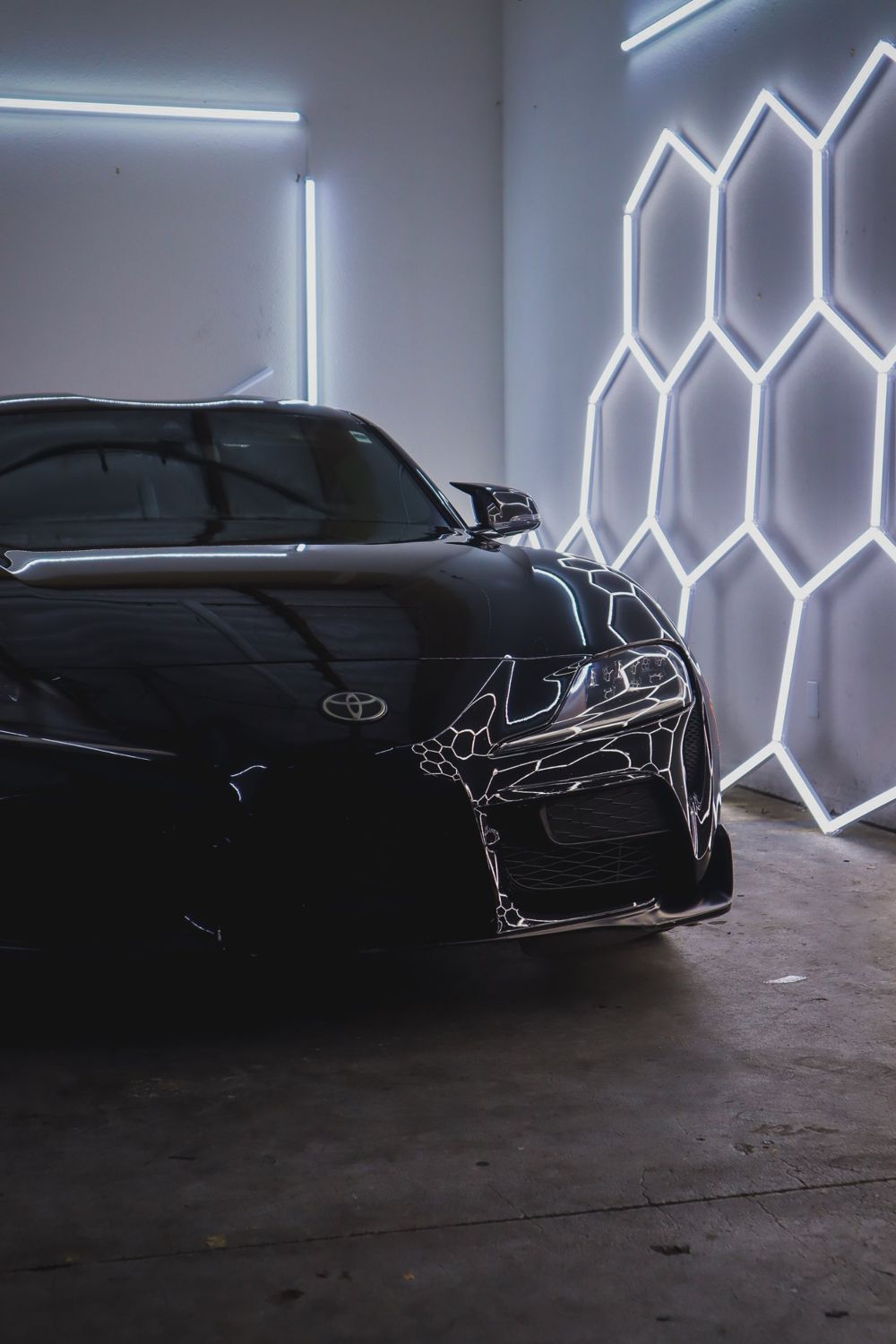 Front corner of a black 2020 Toyota GR Supra wrapped in Gloss Black Obsidian color PPF by Drift Wraps in Rancho Cordova under hexagon lights