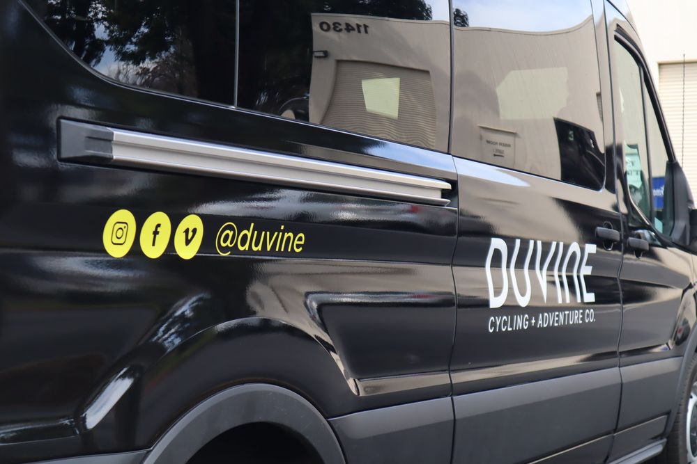 Logo and social handles on the side of a DuVine Cycling + Adventure Co. Ford Transit van with a full wrap and custom decal text by Drift Wraps in Rancho Cordova
